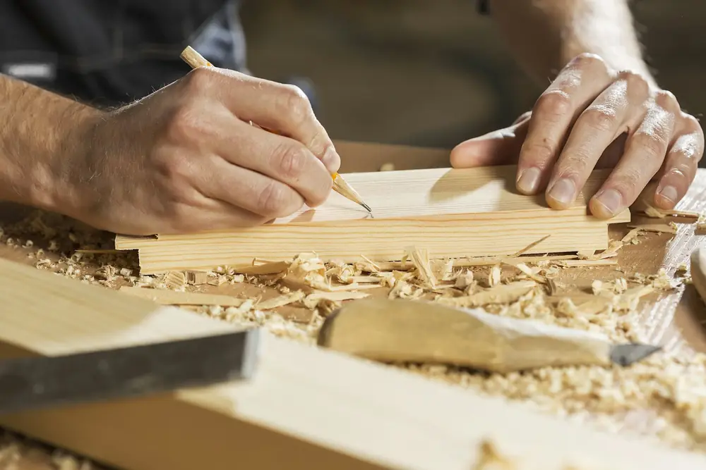 Hands measuring and marking a piece of wood in a workshop